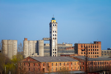 Obraz premium Abandoned damaged old granary against town and blue cloudy sky