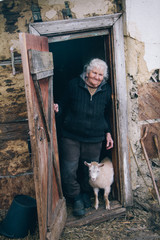 A very old woman with gray hair in old clothes stands on the threshold of a dilapidated house with...