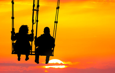 Couple (silhouettes of woman and man) on a seesaw swinging and flying high to sunset. Huge yellow...