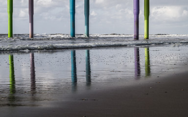 Colorful pier footings columns on North Sea Scheveningen beach reflecting on a sand during storm with waves breaking and foaming in pastel shades with space for text in the corner  