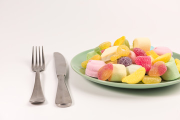 Fork, knife and plate with marshmallow and gummy candies isolated on white background.