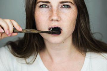 young woman brushing her teeth with a black tooth paste with active charcoal, and black tooth brush...