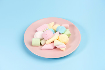 Pink plate with marshmallow isolated on blue background.