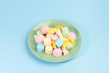 Green plate with marshmallow isolated on blue background. Top view.