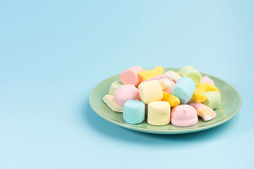 Green plate with marshmallow isolated on blue background.
