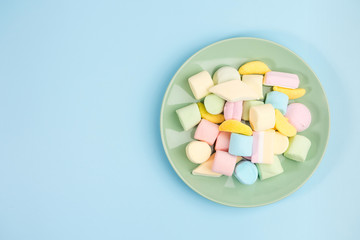 Green plate with marshmallow on blue background. Top view.