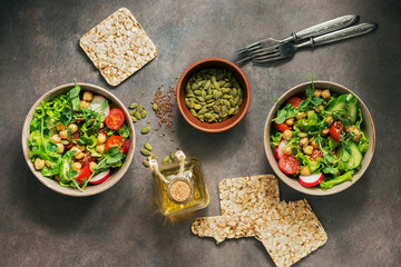 Two bowls of vegan and vegetarian dietary salad of fresh vegetables, chickpeas and seeds on a dark rustic background. View from above.