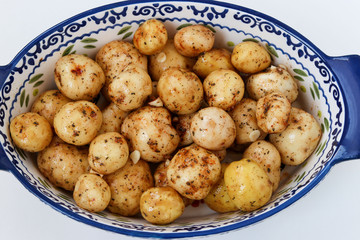 Young peeled potatoes in spices prepared for roasting in a ceramic form on a white background