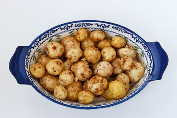 Young peeled potatoes in spices prepared for roasting in a ceramic form on a white background