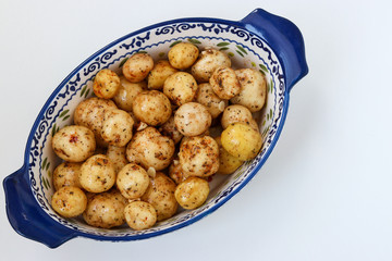 Young peeled potatoes in spices prepared for roasting in a ceramic form on a white background