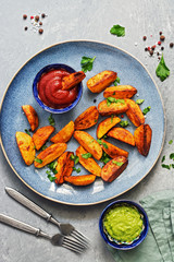 Baked fried potatoes with tomato sauce,guacamole, spices and greens in a plate on a gray background. Top view, copy space.