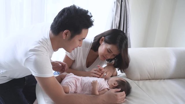 Newborn baby family activity, Asian father and mother are taking care of their sleeping child on sofa. They smile and kiss the child with love. Slow motion footage.