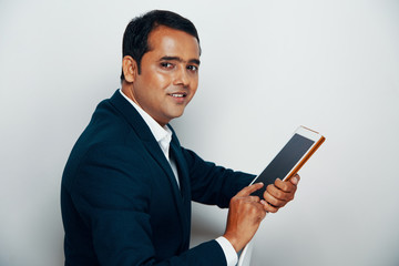 Portrait of Indian professional in suit working online on digital tablet and smiling at camera over white background