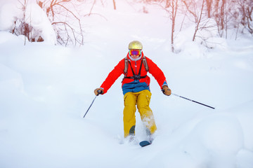 Guy in red jacket and yellow pants rolls down mountain on skis