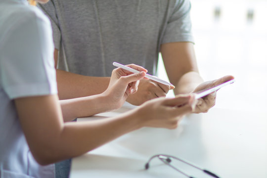 Asian female doctor using tablet computer and talking to male Asian patient