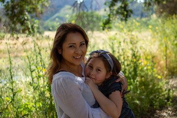 Fototapeta premium Latina Woman and daughter smiling together in front of a bright field at a park