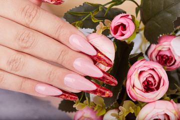 Hand with long red artificial french manicured nails and pink rose flowers