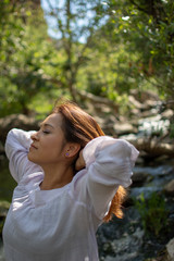 Naklejka premium Latina woman throwing her hair back with her hair in the sun in front of woods and a stream in the shade