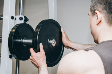 an athlete with big hands adds weight by the metal disks to the training apparatus in the training center. training equipment in the gym close-up