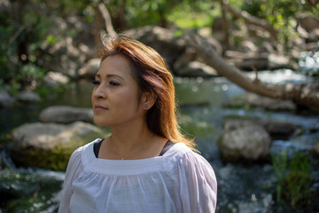 Latina woman with serious expression standing in the shade with glowing hair in a stream with waterfalls in the background