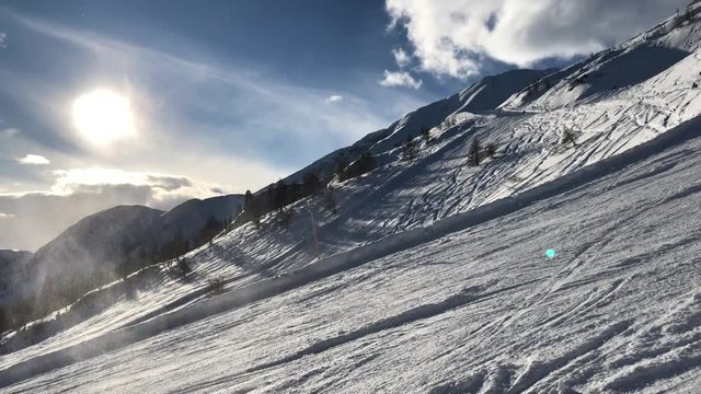 Shot on a ski slope in Flachau, Austria, with people skiing down the snowy mountains near some trees, on a sunny evening with some clouds