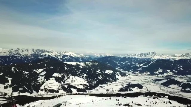 Panoramic shot above Flachau, Austria, with snowy mountains and trees, near a ski slope, on a sunny day with some clouds