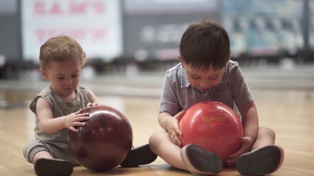Slow motion shot of two kids holding bowling balls and smilling - beautiful toddlers, children.
