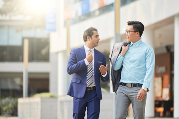 Two businessmen walking along the street and discussing some information after business presentation in the city