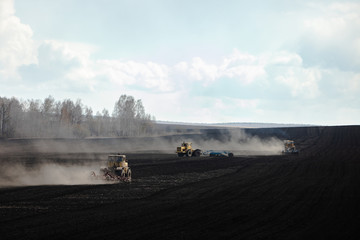 Early in the morning several tractors plow the land in large fields. Spring plowing before planting the crop.
