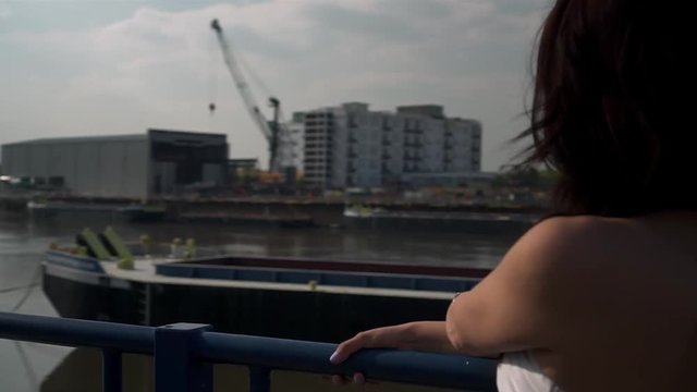 Slow Motion of a Beautiful latina woman on holiday leaning against the railing, looking at the river Thames in London, looking at the camera, smiling and wandering around.
