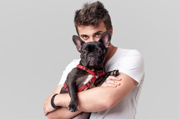 Hipster Bearded guy holding and hugging a nice French Bulldog dog in his arms with love and playing...