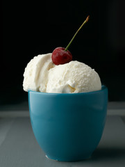 Cup with balls of ice cream with a cherry on a dark background