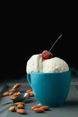 Balls of ice cream in a blue cup and almond nuts with walnuts on a dark background with copy space