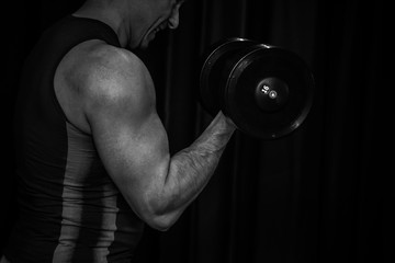Fototapeta na wymiar athlete trains biceps hands with dumbbells in the center of workouts on a black background. training tools in the gym close-up