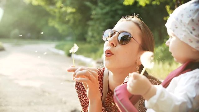 Mother and baby girl blowing on a dandelion flower in the summer in the park