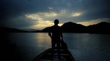 On a calmness lake, a lonely people with a guitar look round to the scenic landscape, from a wooden boat. - Powered by Adobe