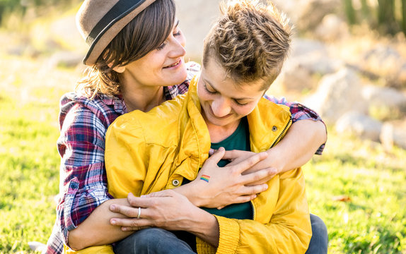 Young girlfriends in love sharing time together at travel trip hugging at park - Playful women friendship concept with girls couple having fun on fashion clothes outdoors - Bright warm sunshine filter