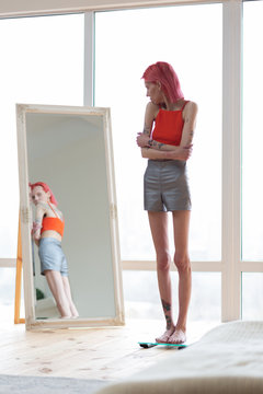 Skinny unhealthy woman wearing shorts and top looking into mirror
