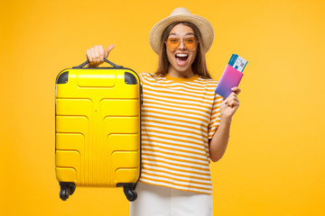 Happy European girl with suitcase and airplane tickets isolated on yellow background excited about...