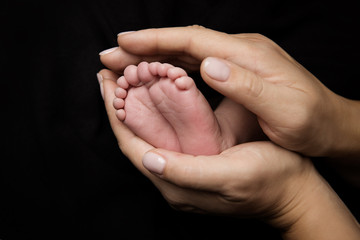 Feet of Newborn Baby, Mother Holding New Born Kid Legs in Hand, Black Background
