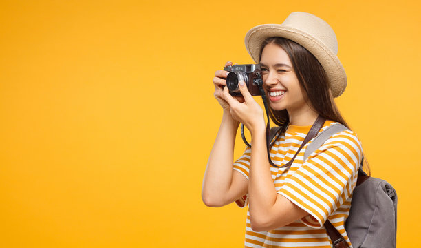 Good-looking Caucasian girl taking pictures with retro camera on vacation isolated on yellow background, copyspace on left