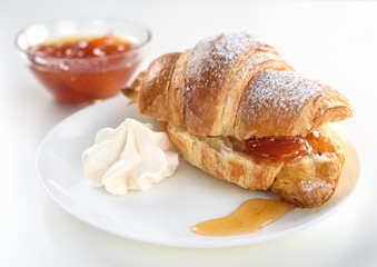 Cut croissant with apricot jam on a white plate with a meringue.