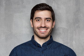 Headshot portrait of smiling young man isolated on gray wall background