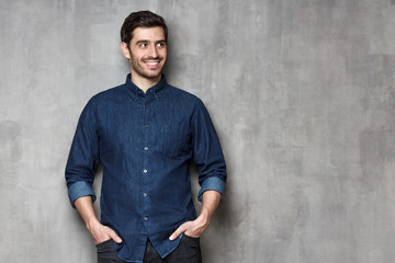 Obraz premium Relaxed stylish guy smiling happily while having rest, isolated on gray textured wall