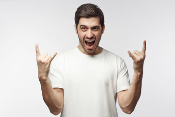 Young man showing rock sign with his fingers as if listening to favourite music, isolated on white background