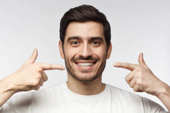 Young smiling man pointing at his perfect white teeth with two index fingers