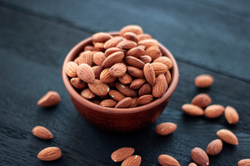 Almonds nuts in ceramic bowl on on the dark oak texture