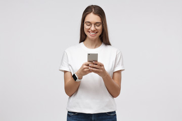 Fototapeta premium Young attractive european female with smartphone in hands, isolated on gray background