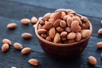 Almonds nuts in ceramic bowl on on the dark oak texture