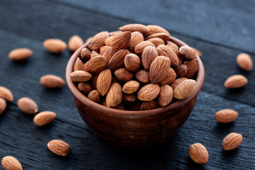 Almonds nuts in ceramic bowl on on the dark oak texture